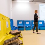 Kobieta stojąca na tle żółtych i niebieskich pojemników. 