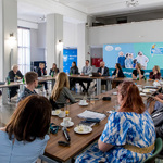 Uczestnicy II spotkania grupy roboczej ds. Regionalnych Planów Adaptacji do Zmian Klimatu siedzący na sali przy stole, w tle prezentacja