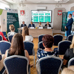 Publiczność słucha panelu dyskusyjnego o Regionalnym Planie Adaptacji do zmian klimatu dla Województwa Śląskiego, na sali obecni są dziennikarze i prelegenci.