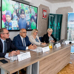 Panel konferencji w Krzepicach – czterech prelegentów siedzi przy stole, w tle ekran z dziećmi trzymającymi zielone balony.