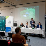 Panel konferencji o adaptacji do zmian klimatu, na ekranie wyświetlona fotografia przyrody, Burmistrz Czechowic-Dziedzic omawia wyświetlaną prezentację.