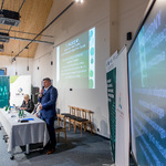 Przewodniczący Sejmiku Województwa Śląskiego przemawia przy użyciu mikrofonu podczas prezentacji, obok niego siedzą pozostali uczestnicy konferencji.