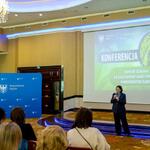 Ewa Owczarek-Nowak – Dyrektor Departamentu Ochrony Środowiska, Ekologii i Opłat Środowiskowych Urzędu Marszałkowskiego Województwa Śląskiego wita gości zgromadzonych na sali konferencyjnej, na ekranie slajd z tytułem ‘Konferencja – wspólne działania na rzecz poprawy jakości powietrza w województwie śląskim’; w tle niebieska ścianka z herbem województwa.