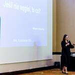 prelegentka - dr Katarzyna Korszun-Kłak z referatu ds. planowania w zakresie środowiska w Departamencie Ochrony Środowiska, Ekologii i Opłat Środowiskowych Urzędu Marszałkowskiego Województwa Śląskiego trzyma mikrofon w sali konferencyjnej, na ekranie slajd z napisem ‘Jeśli nie węgiel, to co?’ oraz datą i miejscem spotkania