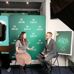 Studio nagraniowe „Climate Voices Studio”. Dwie osoby siedzą na krzesłach przed zielonym tłem z logo „CLIMATE-CON”. Po lewej stronie widoczna kamera z podglądem nagrania, po prawej duża lampa studyjna. Obok stoi plansza z napisem „Climate Voices Studio”