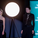 Dwie osoby w czarnych strojach prezentują biżuterię na tle planszy „Climate-Con” i dużego okrągłego światła