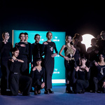 Zespół osób w czarnych strojach pozuje na scenie przed planszą „Climate-Con” i reflektorami