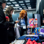 Grupa osób przy stoisku z kolorowymi pudełkami „Śląskie. Dla Seniora” i „Śląskie. Dla kobiety” gadżetami promocyjnymi