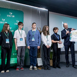 Kilka osób na scenie trzyma duży voucher podczas prezentacji nagród na tle planszy „Climate-Con”