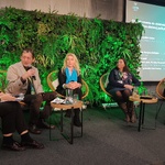 Panel dyskusyjny z pięcioma osobami na scenie, w tle zielona ściana z roślin i ekran z prezentacją